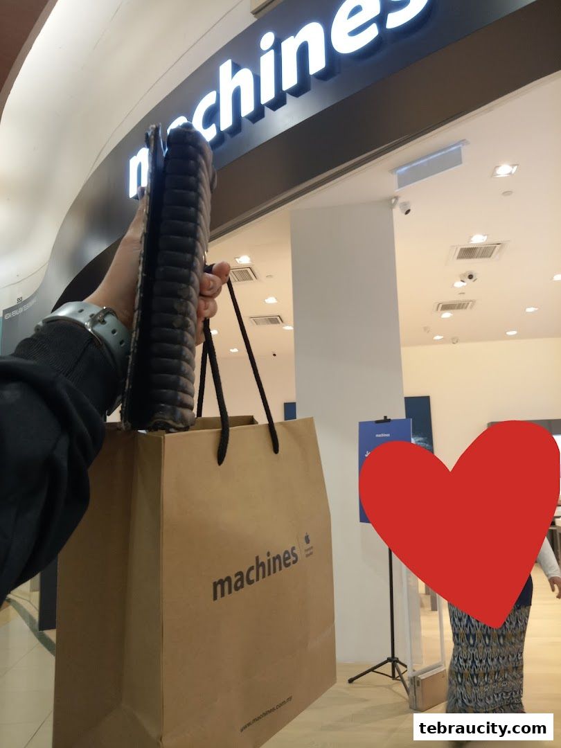 A person holds a shopping bag and a tablet in front of the Machines Apple Reseller Store.