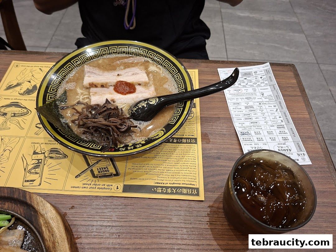 A bowl of ramen with pork, seaweed, and mushrooms, next to a drink and an order sheet.