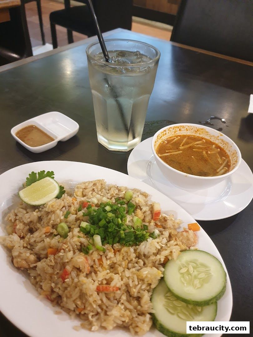 A plate of fried rice with a side of soup and a glass of iced drink.