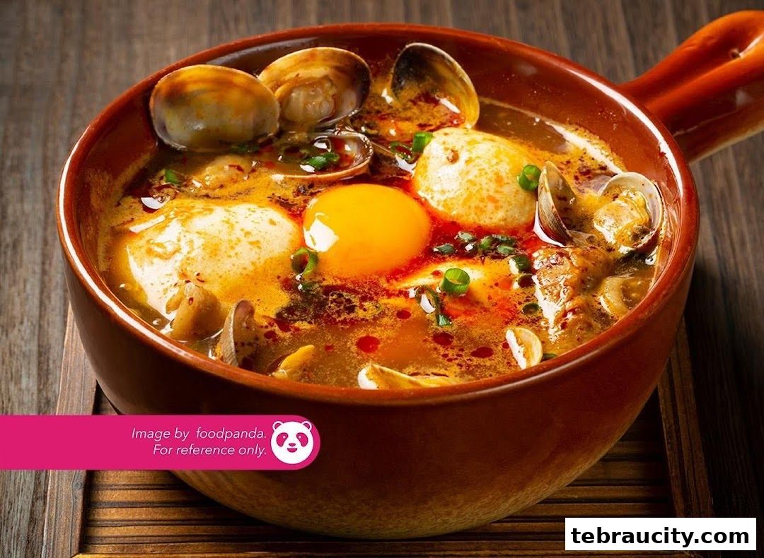 A close-up of a steaming bowl of Korean stew with clams, tofu, and a cracked egg.