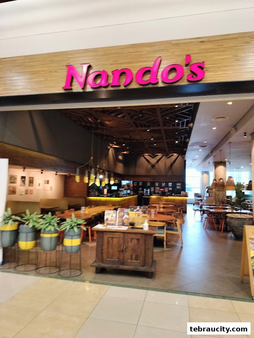 The entrance to a Nando's restaurant with its signature pink logo and interior seating visible.