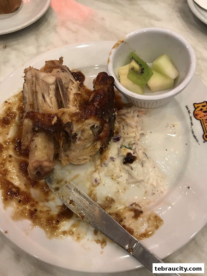 A plate of roasted chicken with coleslaw and fruit, partially eaten.