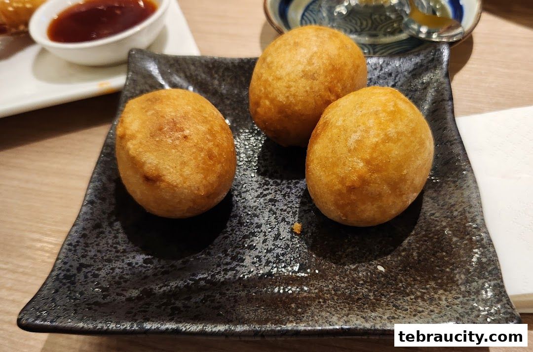 Three golden-brown fried balls served on a dark textured plate with a side of dipping sauce.
