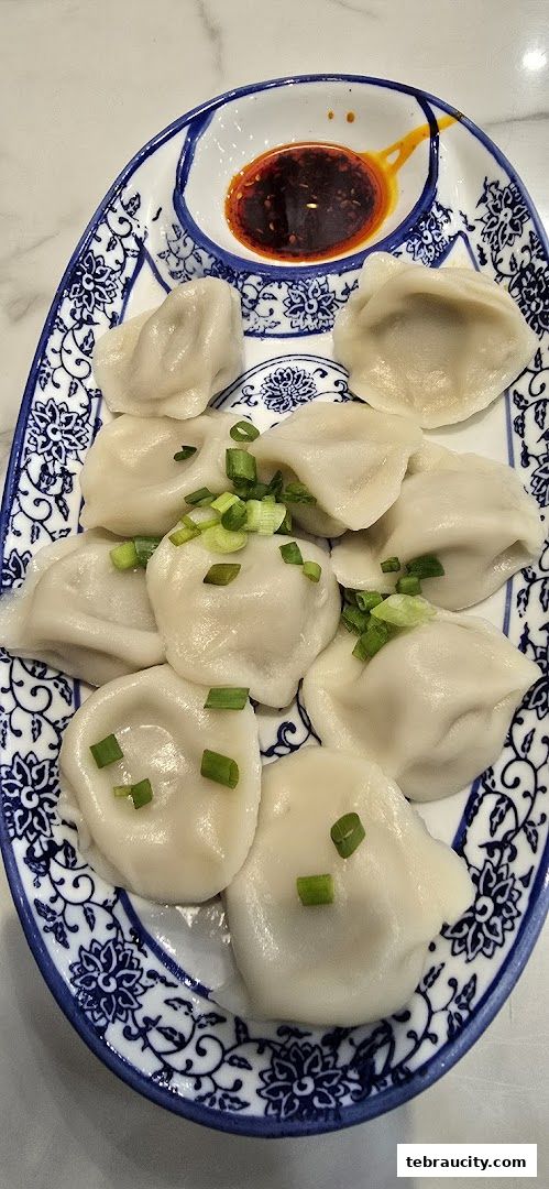 A plate of steamed dumplings garnished with chopped green onions and a side of chili oil.