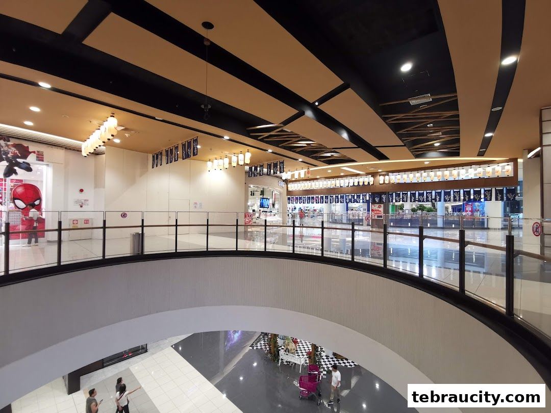 Interior view of a shopping mall with shops and escalators, featuring a Spiderman display.