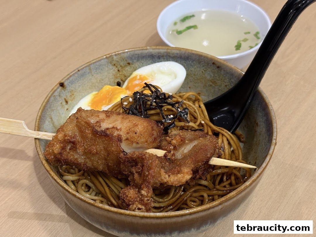 A bowl of noodles with fried chicken, egg, and a side of soup.