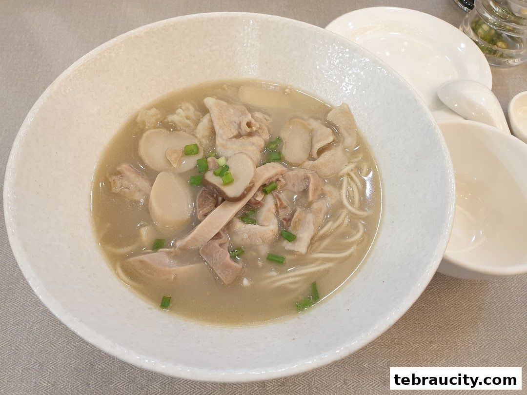 A close-up shot of a steaming bowl of noodle soup with pork and mushrooms.