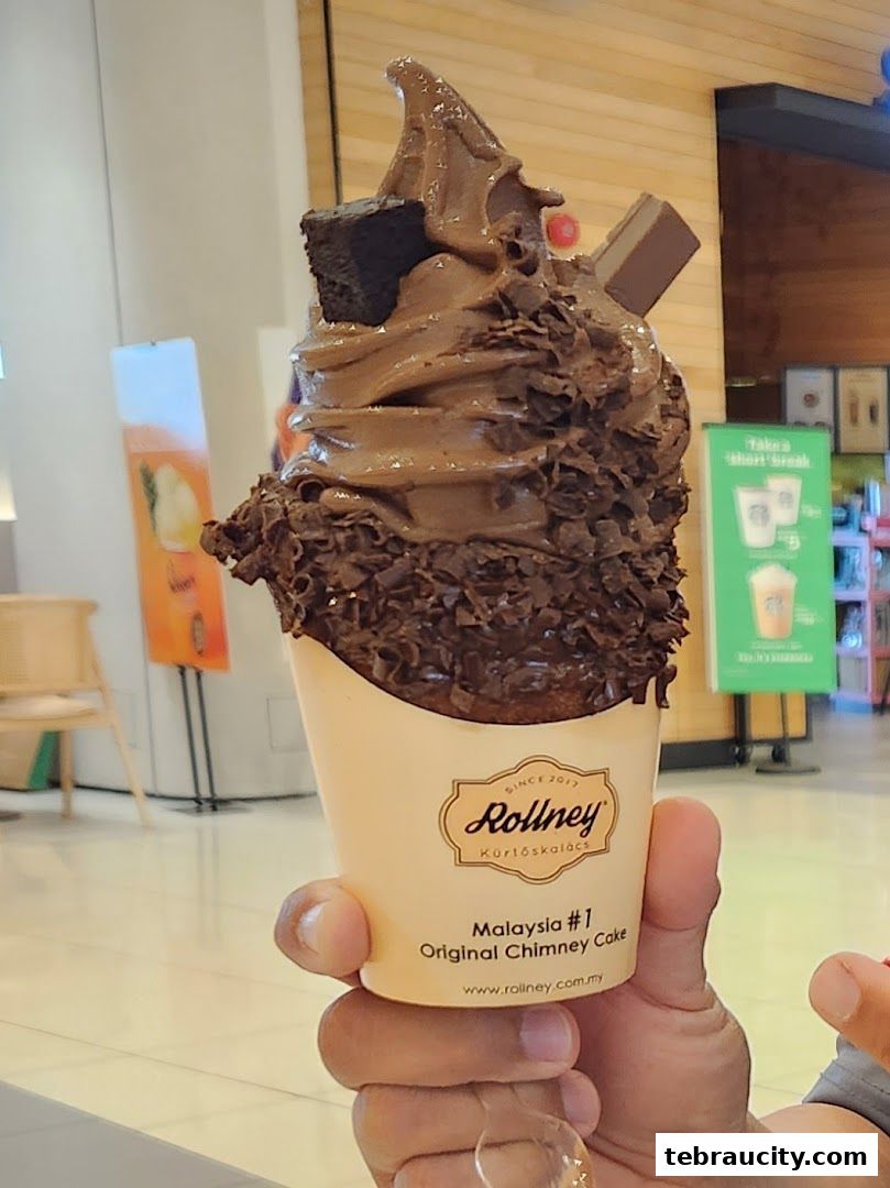 A person holds a chocolate chimney cake with brownie and chocolate shavings.