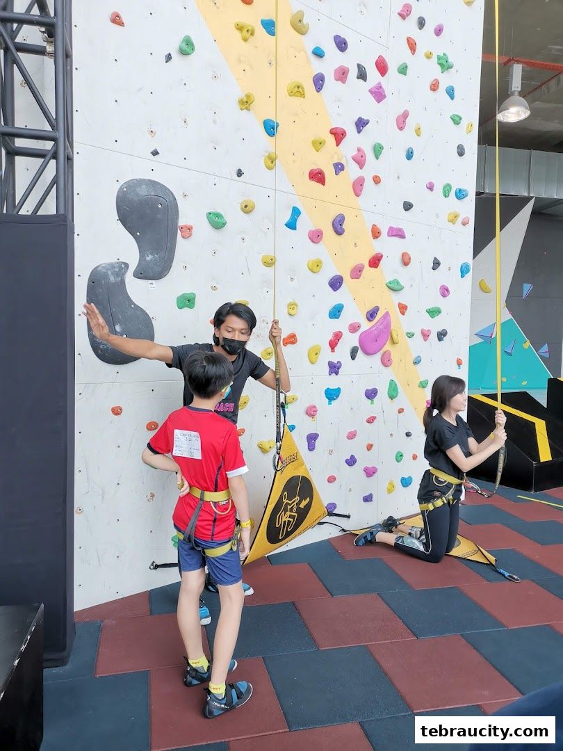 An instructor guides two children on a colorful indoor climbing wall.