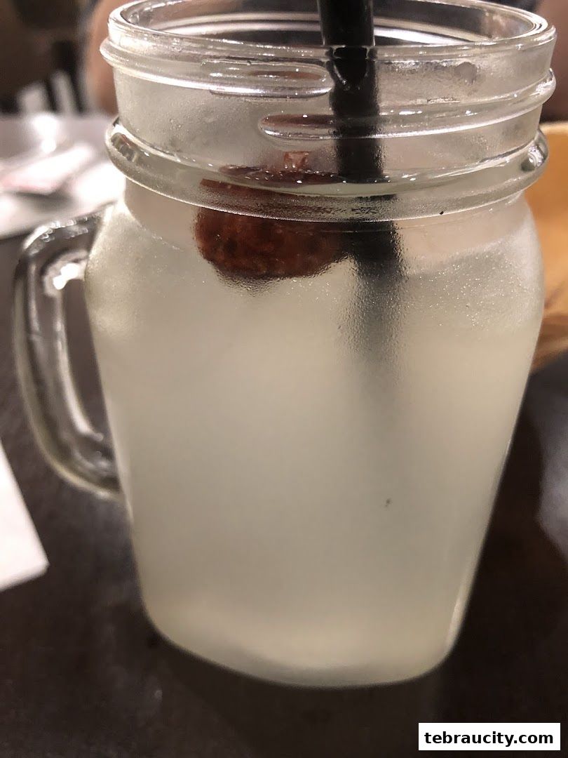 A close-up shot of a refreshing beverage in a glass jar with a straw and a piece of fruit.