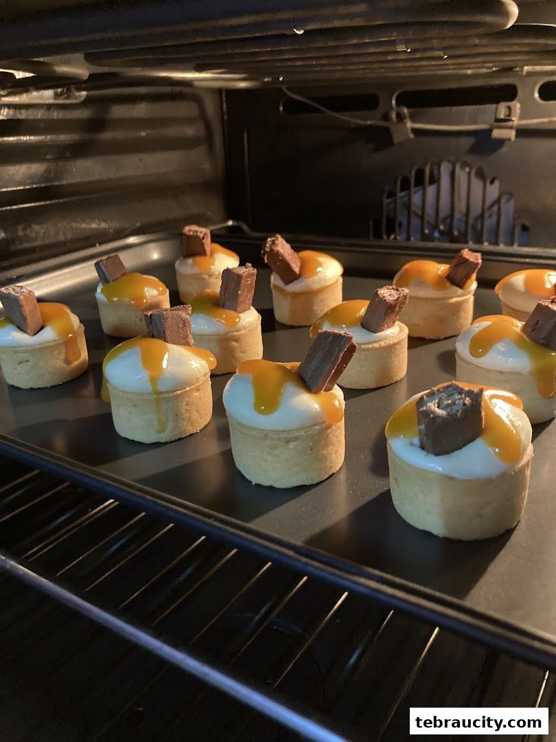Mini tarts with white cream, caramel sauce, and chocolate pieces baking in an oven.