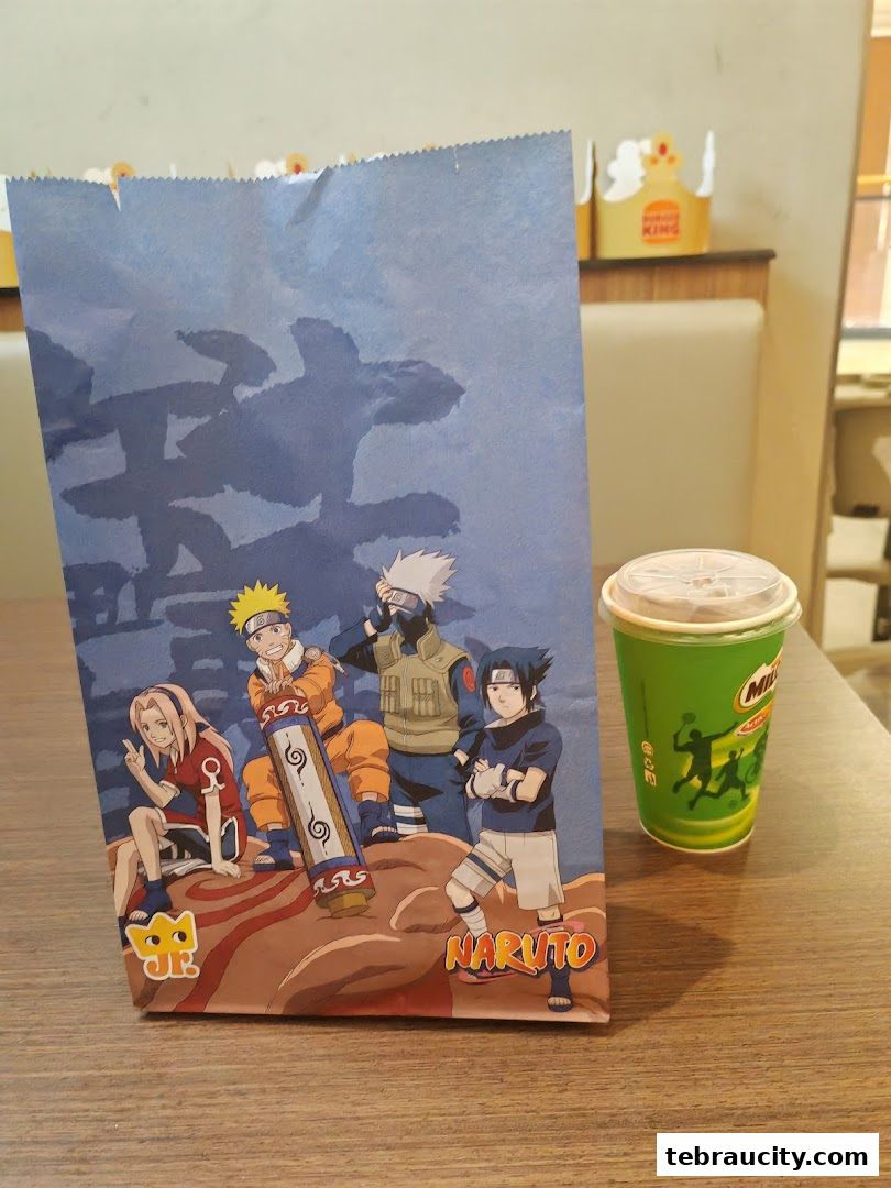 A Burger King paper bag with Naruto characters and a Milo drink on a table.
