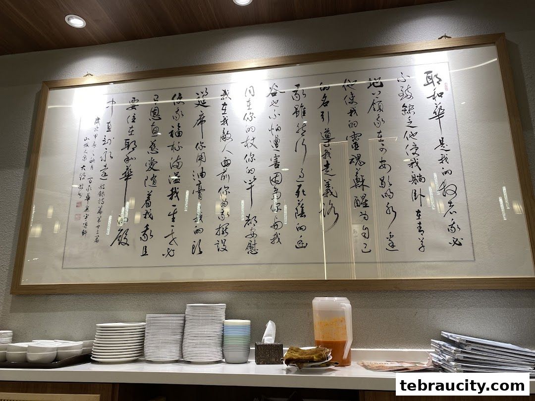 A framed calligraphy artwork hangs above stacks of plates and a beverage dispenser.