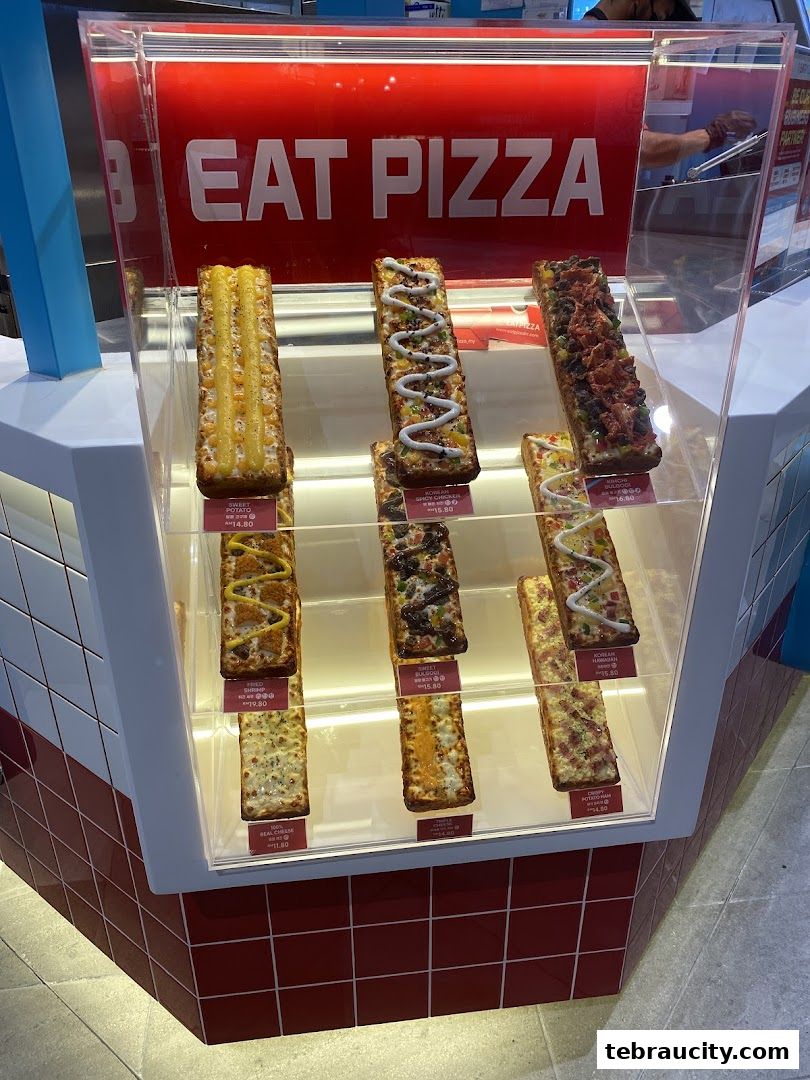 A display case showcasing various rectangular pizzas with different toppings and prices.