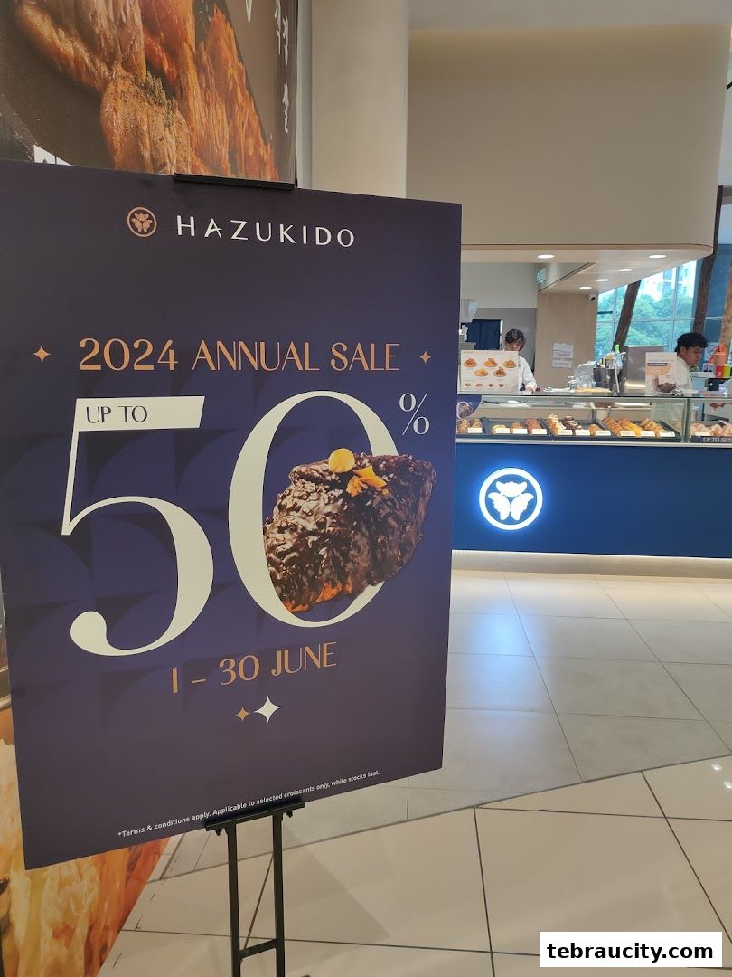 A sign advertising a 50% annual sale at Hazukido Bakery Cafe, with the shop interior visible in the background.
