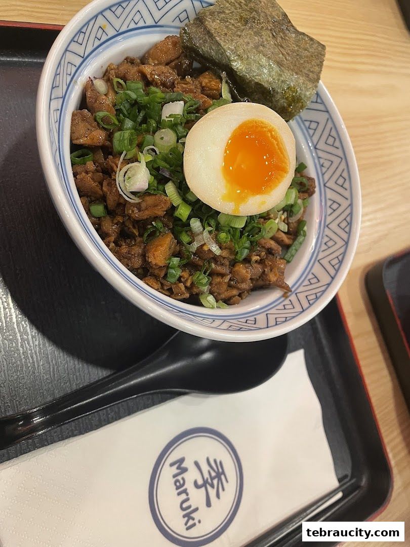 A bowl of Japanese rice with meat, egg, and seaweed, served with a spoon.