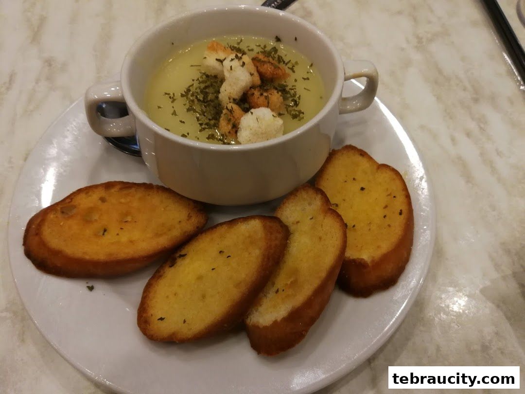 A bowl of creamy soup topped with croutons and herbs, served with toasted bread slices.