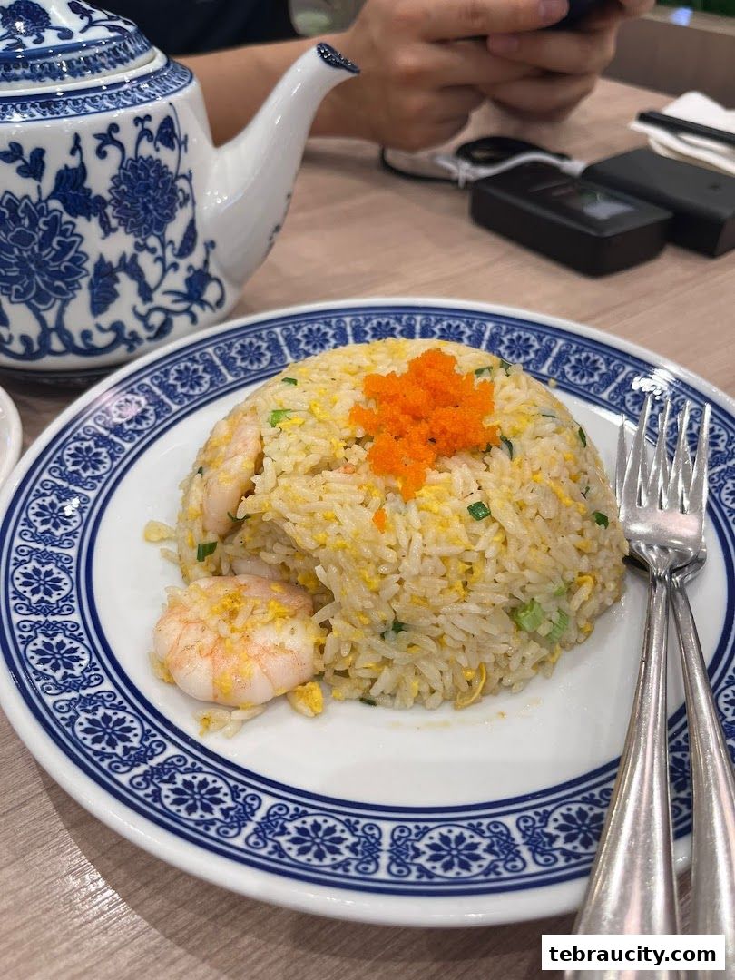 A plate of shrimp fried rice with a teapot and forks on a wooden table.