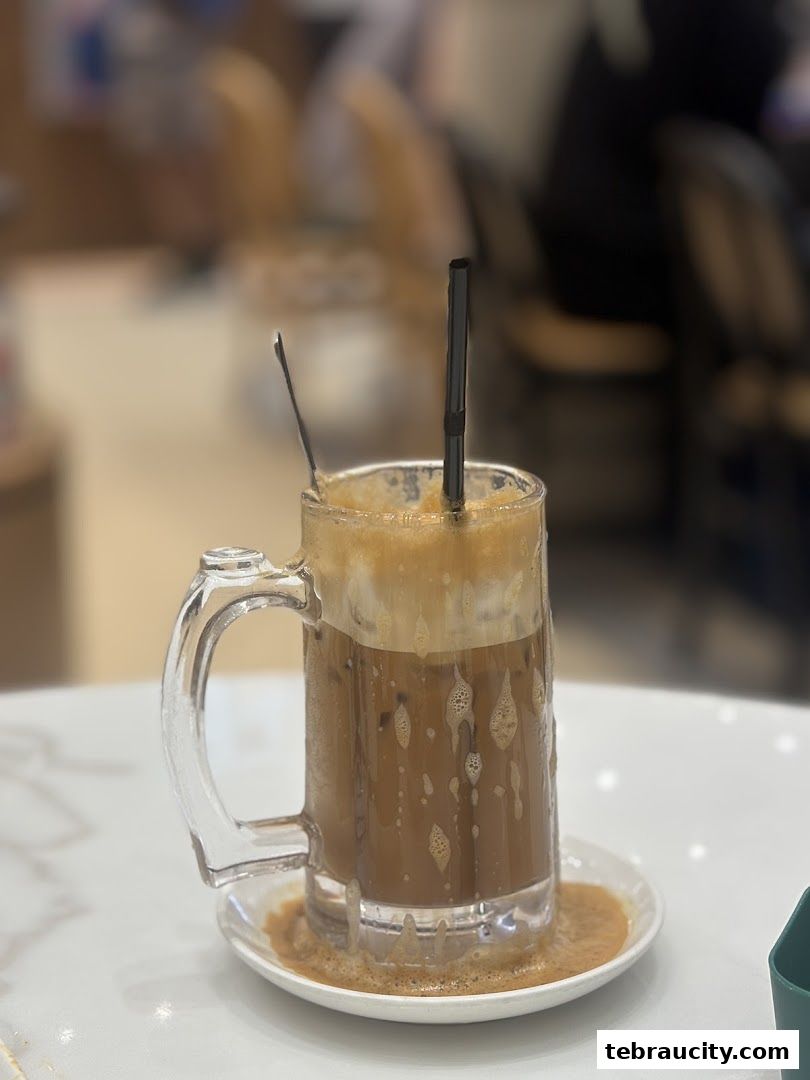 A refreshing iced coffee with foam and a straw in a glass mug on a saucer.
