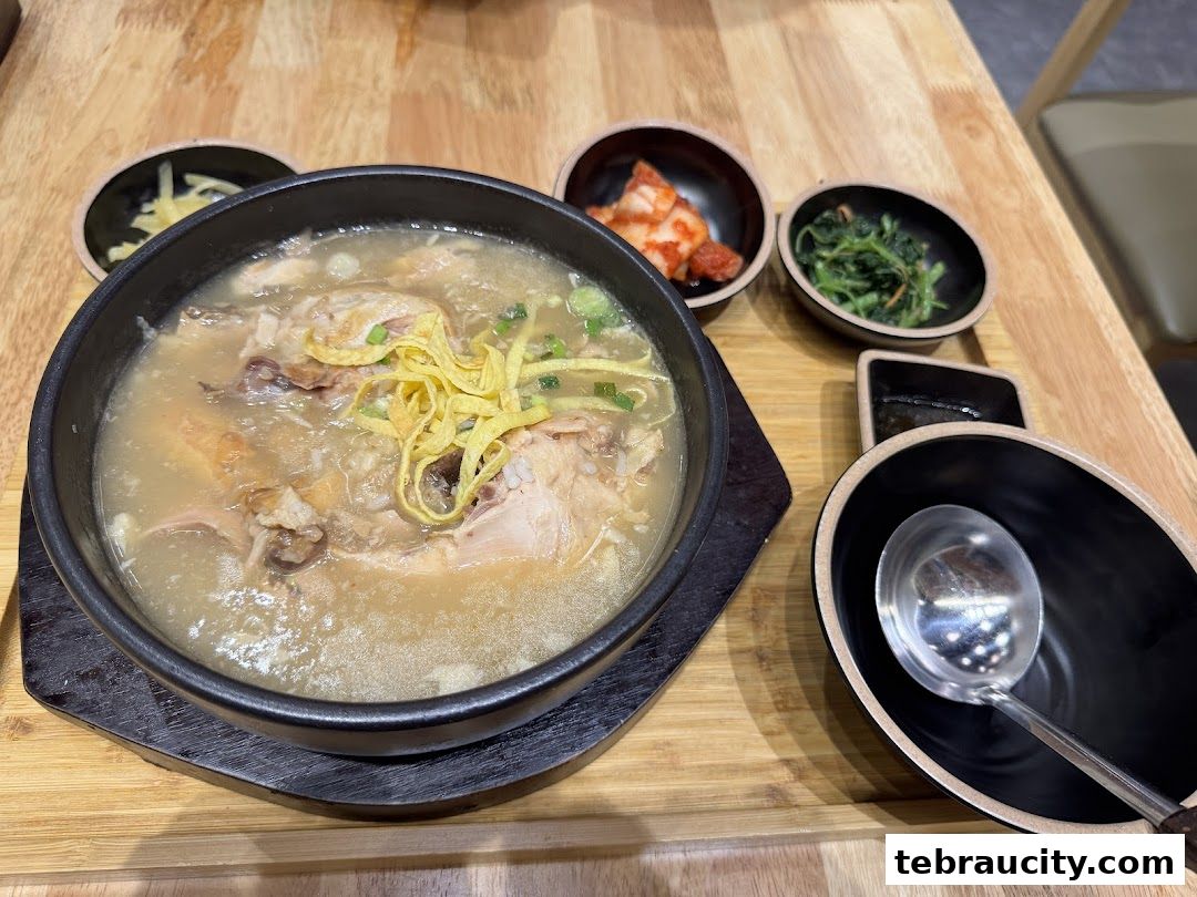 A steaming bowl of Korean chicken soup with side dishes and a ladle.