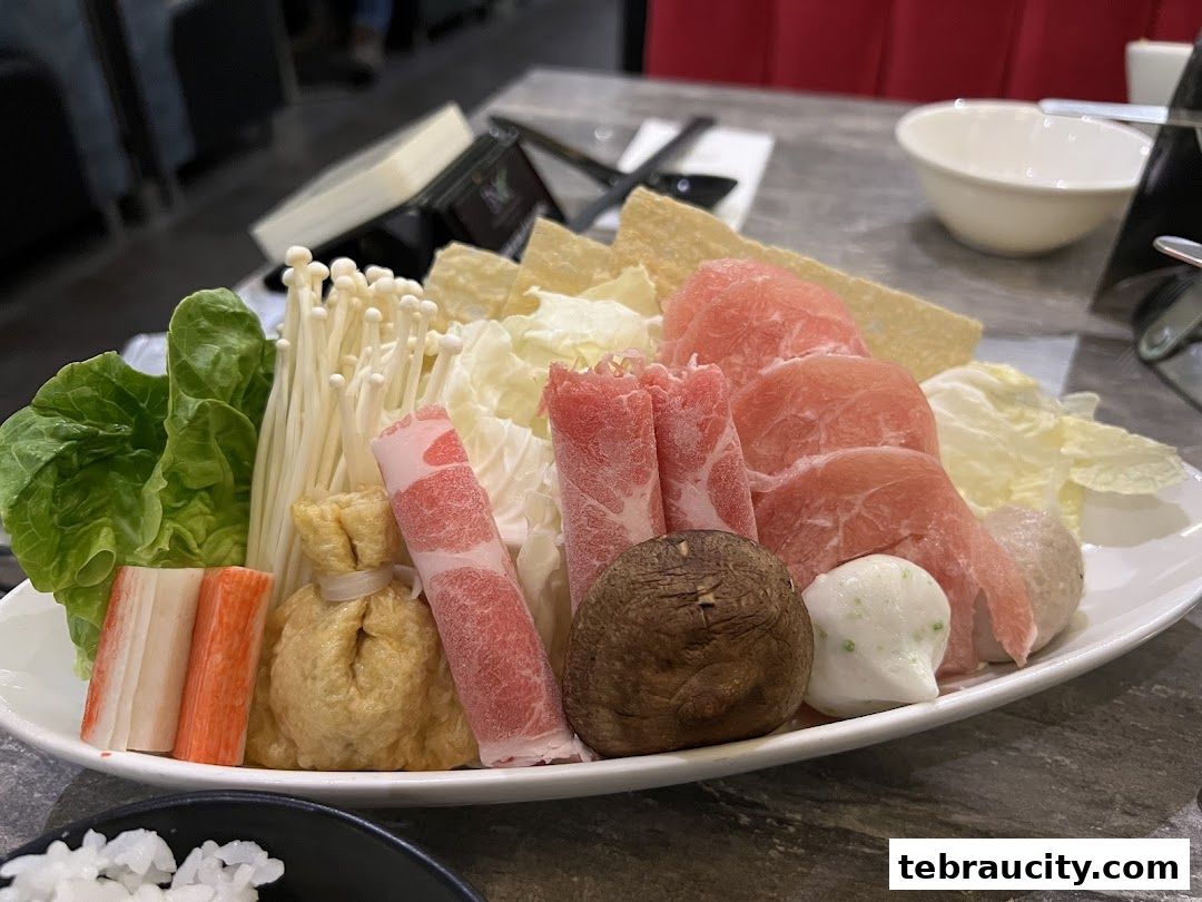 A platter of fresh shabu-shabu ingredients including meat, vegetables, and seafood.
