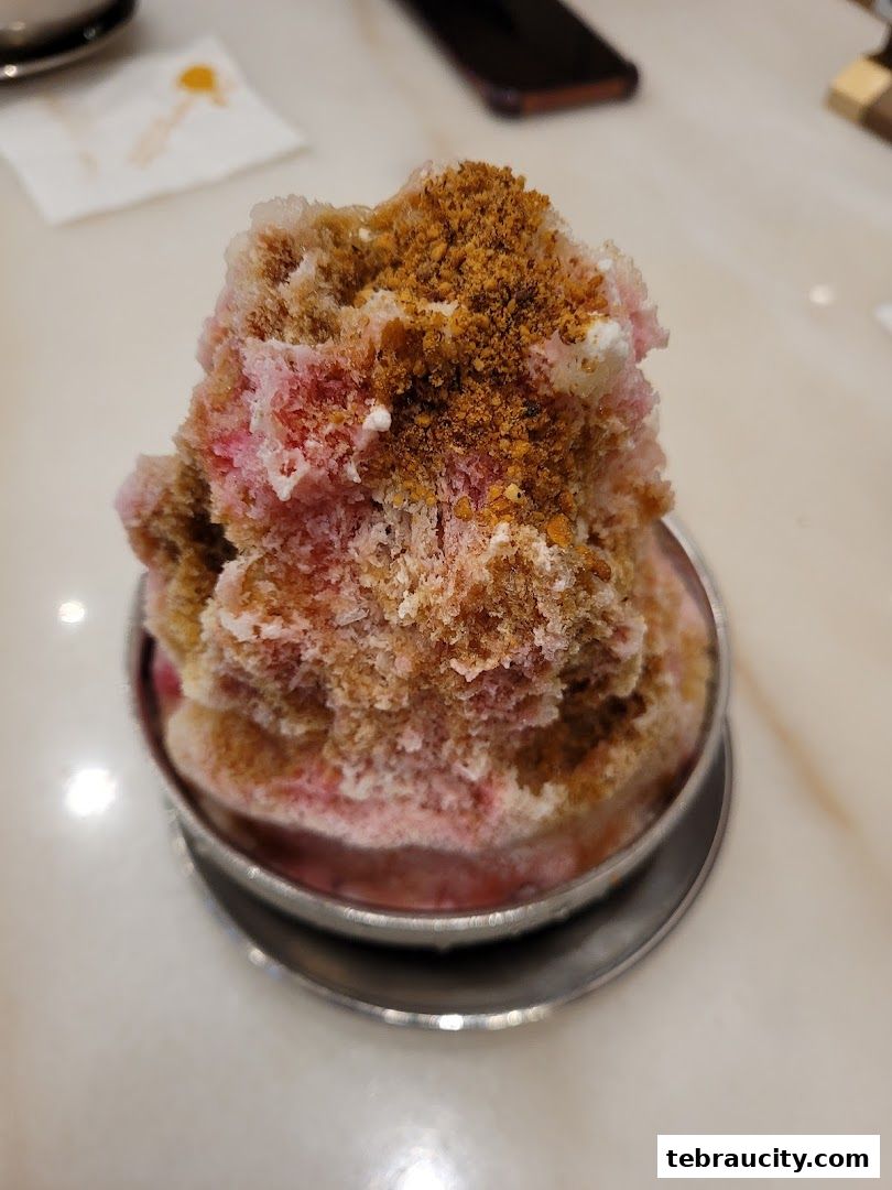 A close-up of a refreshing shaved ice dessert with pink syrup and crunchy toppings.