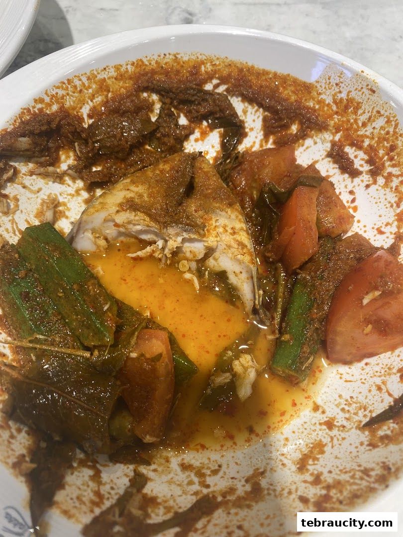 A close-up of a plate of Asam Pedas fish with okra and tomatoes.