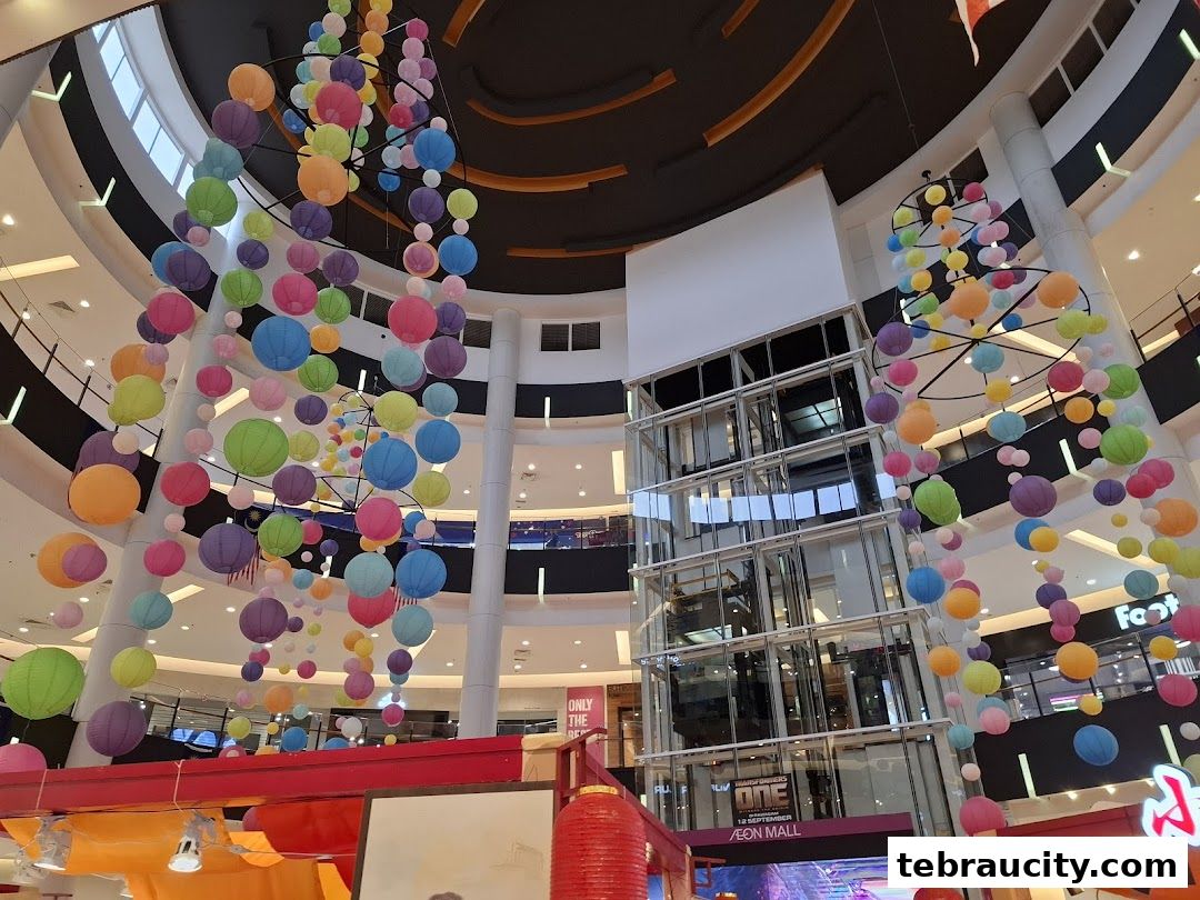A mall atrium decorated with colorful hanging lanterns and a glass elevator.