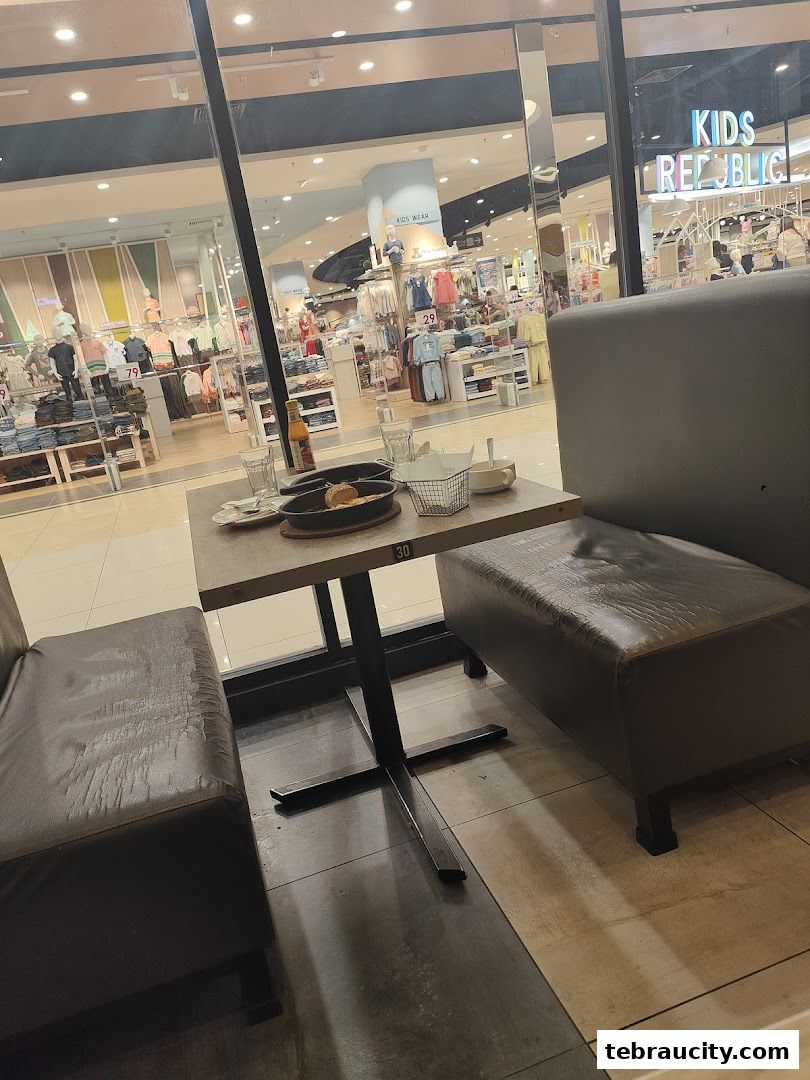 A table with food and drinks set for a meal inside a restaurant, with a view of a clothing store.