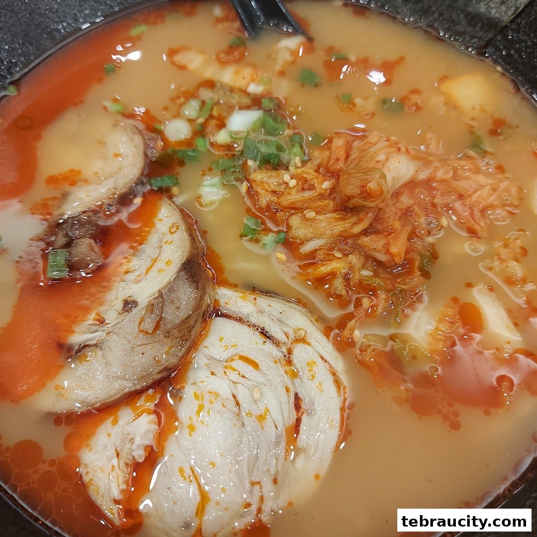 A close-up shot of a steaming bowl of ramen with chashu pork and kimchi.
