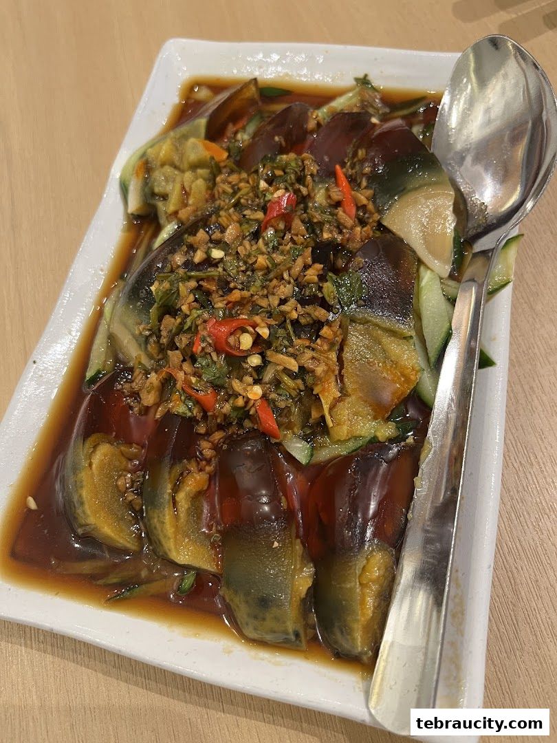 A plate of sliced century eggs with cucumber and a savory sauce, topped with chili and garlic.