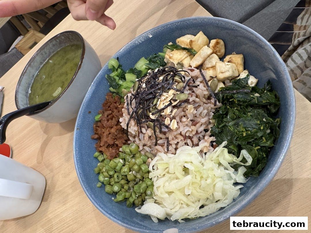 A healthy and colorful bowl of mixed grains, vegetables, and tofu with a side of soup.