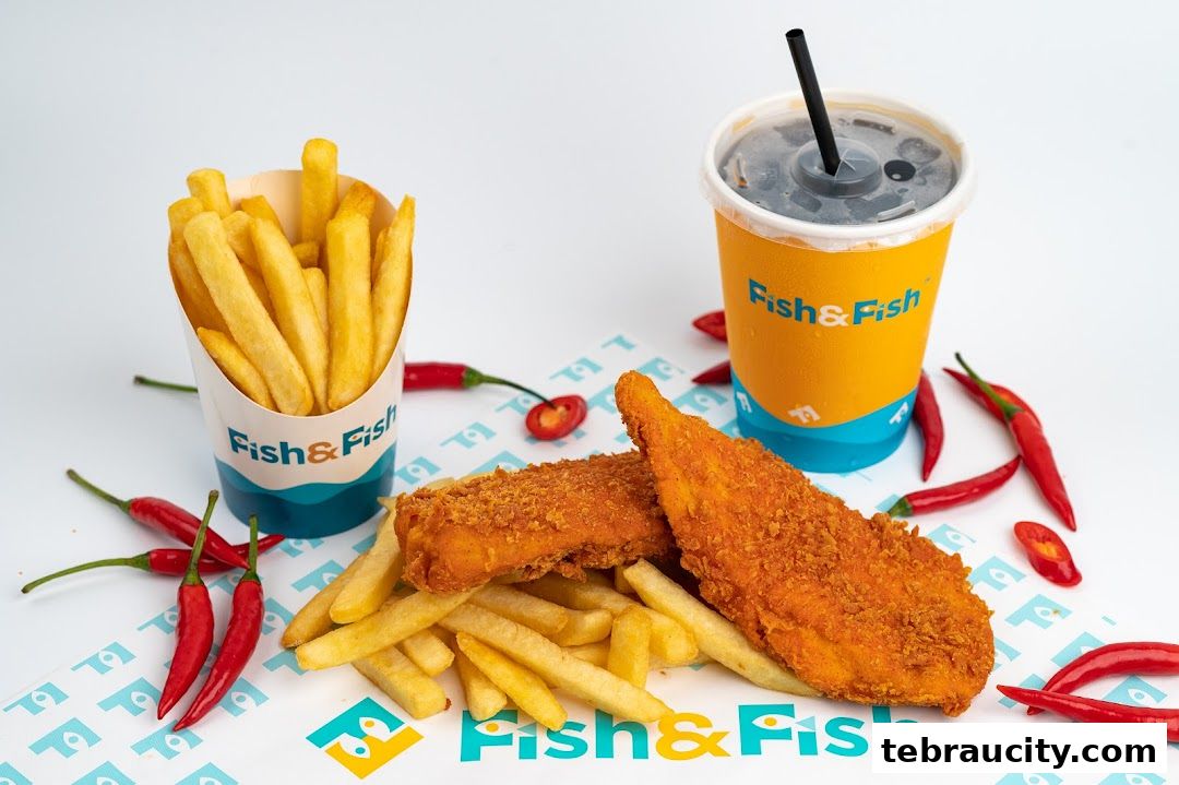 Crispy fish fillets and fries served with a cold drink, garnished with red chilies.