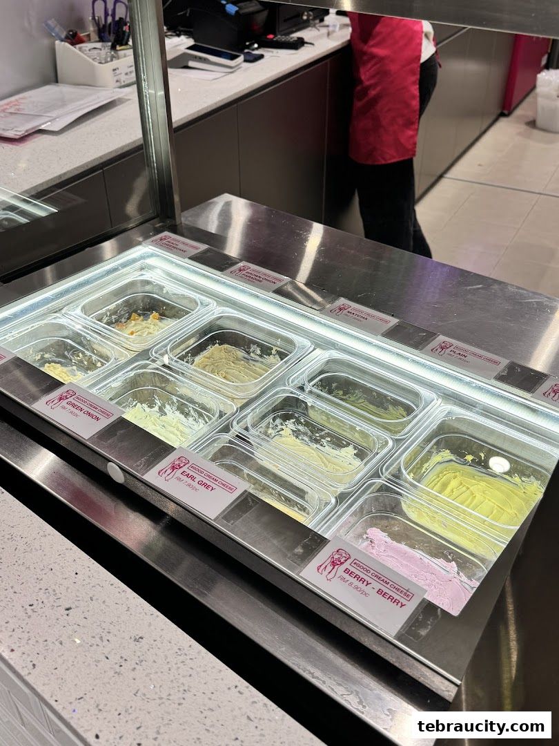 A display of various cream cheese flavors at a bakery counter.