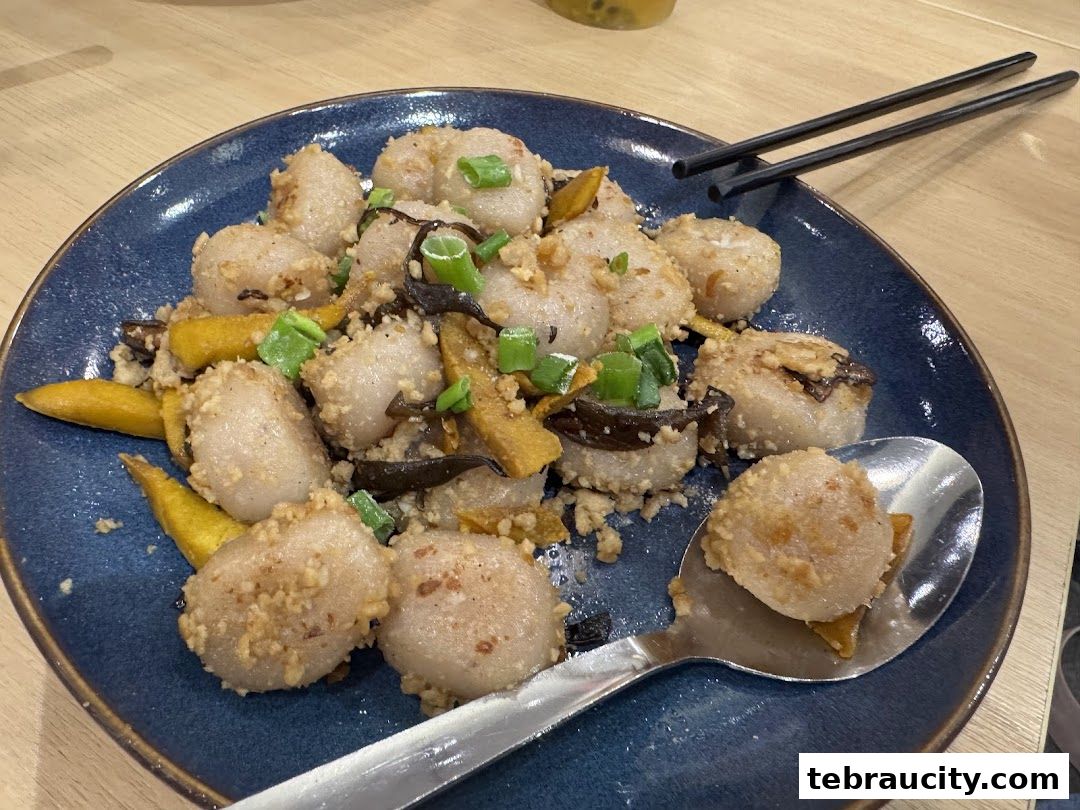 A plate of fried dumplings with chopped scallions and other ingredients, served with chopsticks.