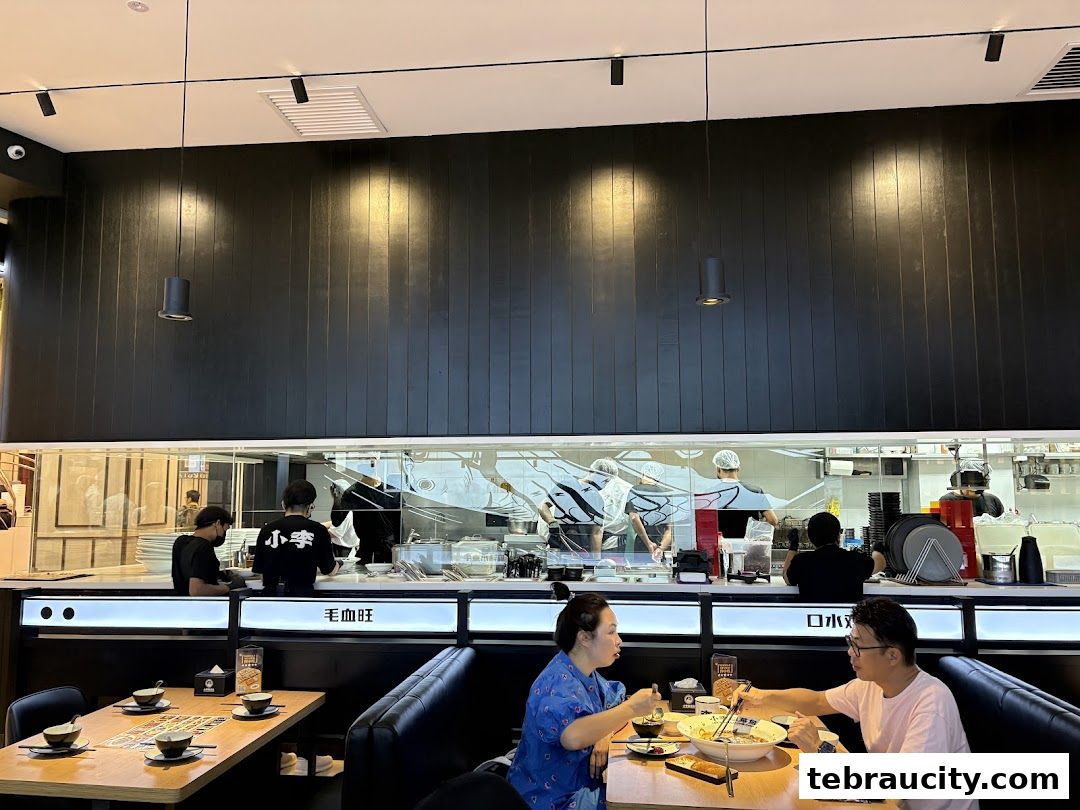 Diners enjoy a meal at Lees Signature Fish, with kitchen staff visible behind a glass partition.