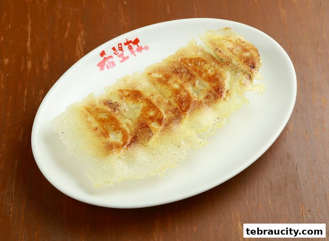 A white oval plate with crispy pan-fried gyoza on a wooden table.