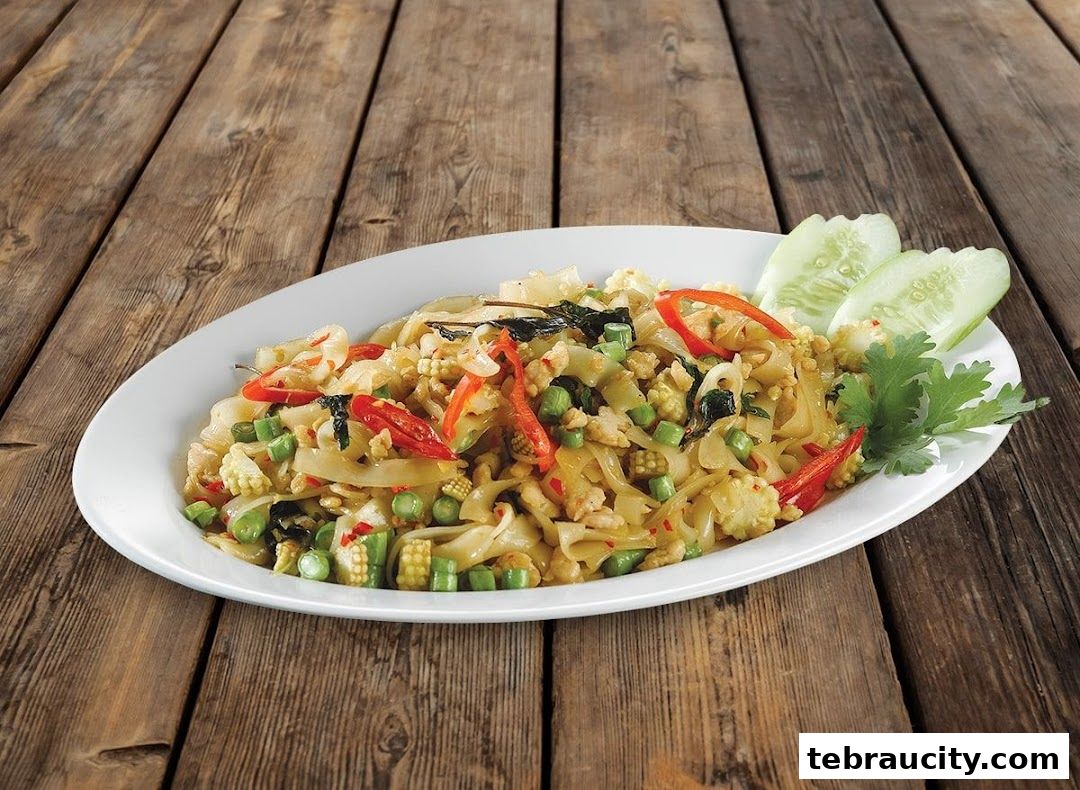 A plate of stir-fried noodles with vegetables and chili on a wooden table.