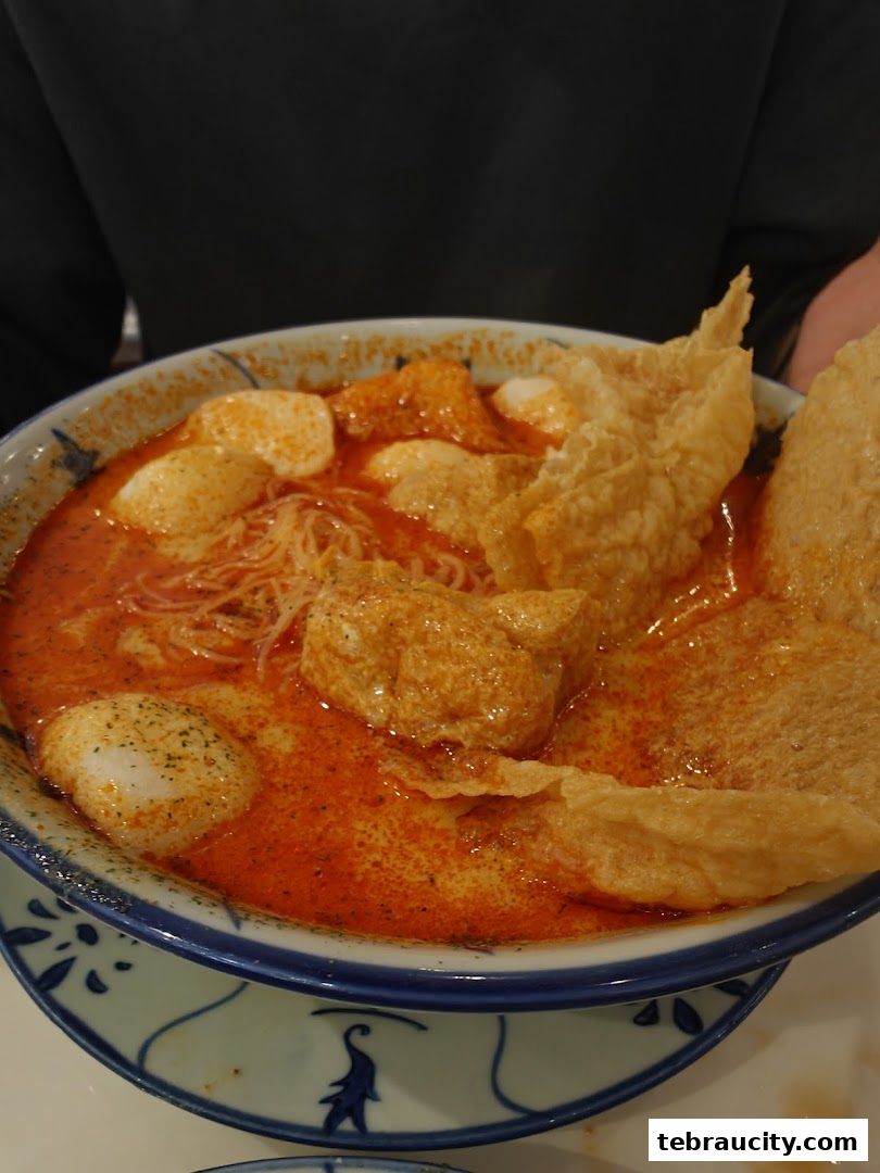 A close-up of a delicious bowl of curry laksa with noodles, fish balls, and crispy wonton skin.