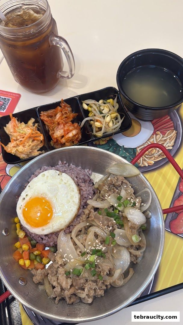 A delicious Korean meal with rice, beef, fried egg, and side dishes, served with iced tea.