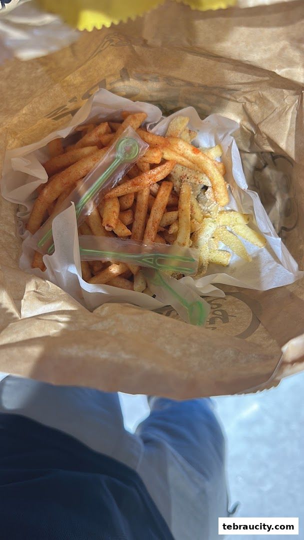 A paper bag filled with seasoned french fries and small green forks.
