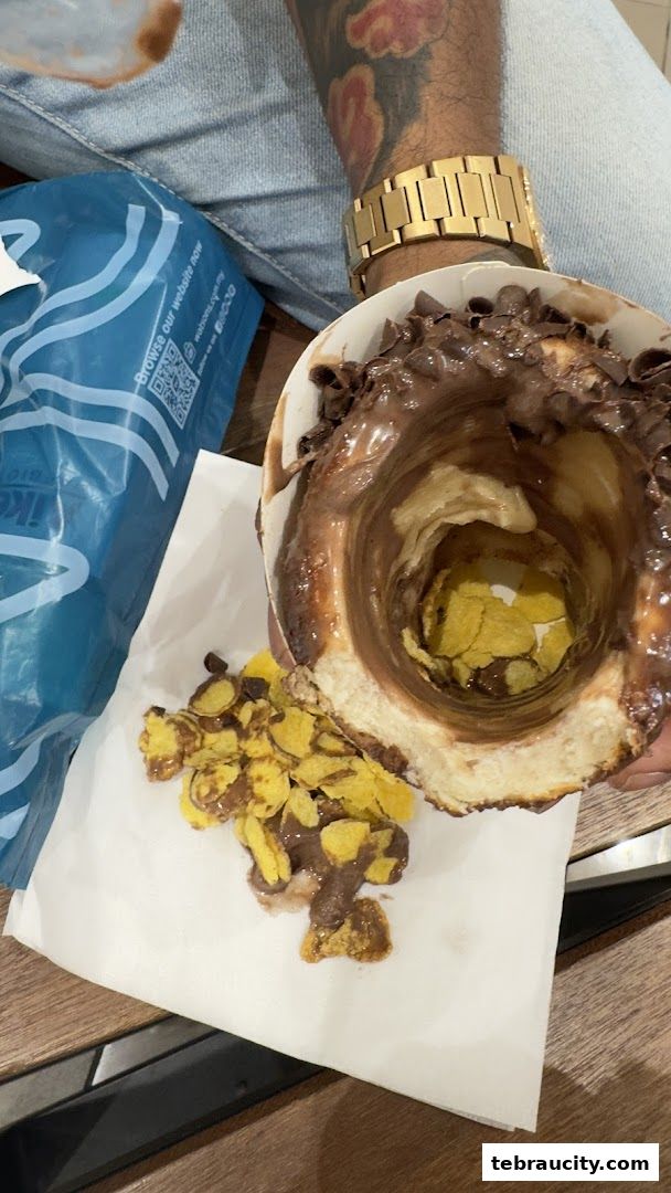 A person holds a dessert filled with chocolate and cornflakes, with a blue bag in the background.