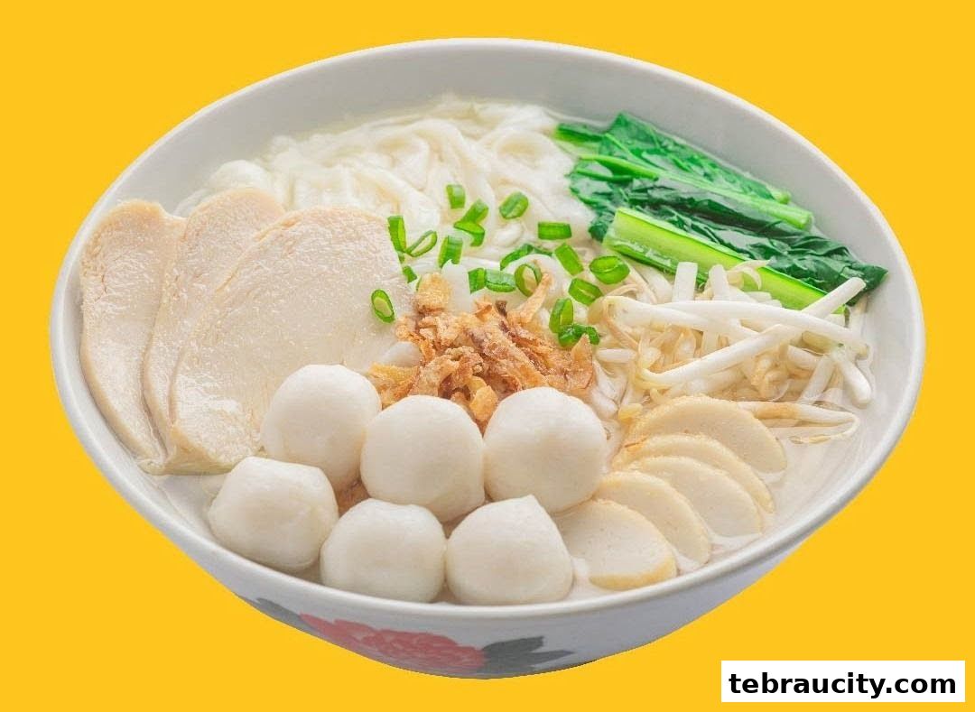 A bowl of noodle soup with chicken slices, fish balls, bean sprouts, and greens.