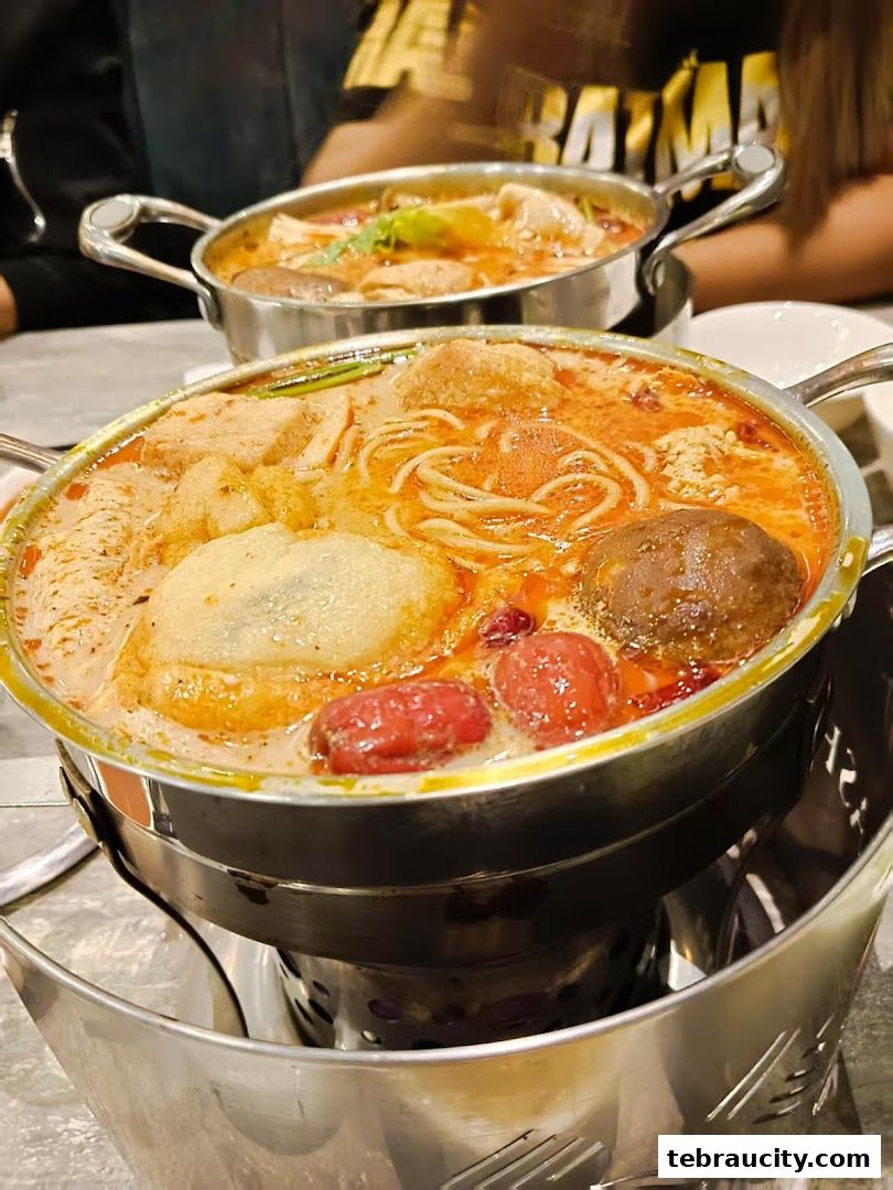 Two steaming pots of shabu-shabu with various ingredients, including noodles and meatballs.