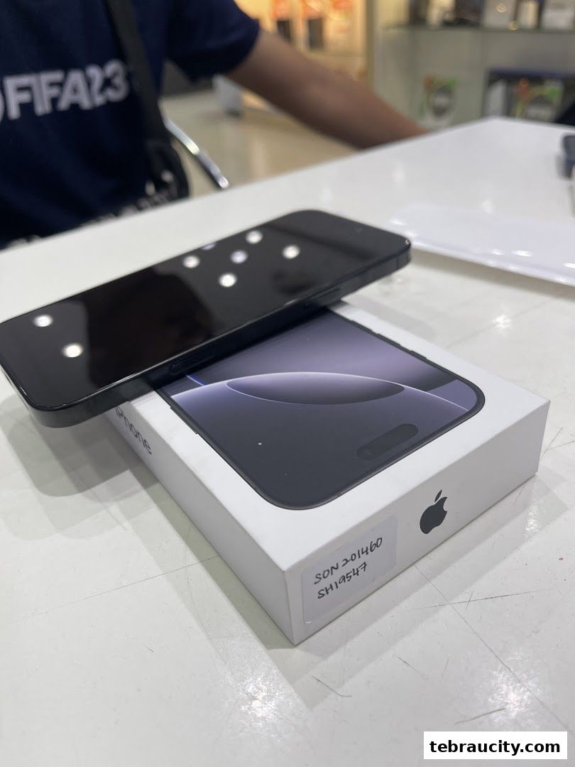 A black iPhone is placed on its box, with a person in the background.