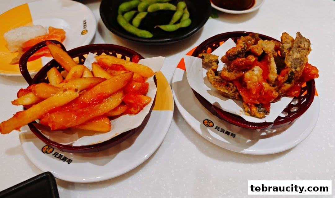 Two plates of food, one with fries and sauce, the other with fried fish and sauce, and edamame in the background.