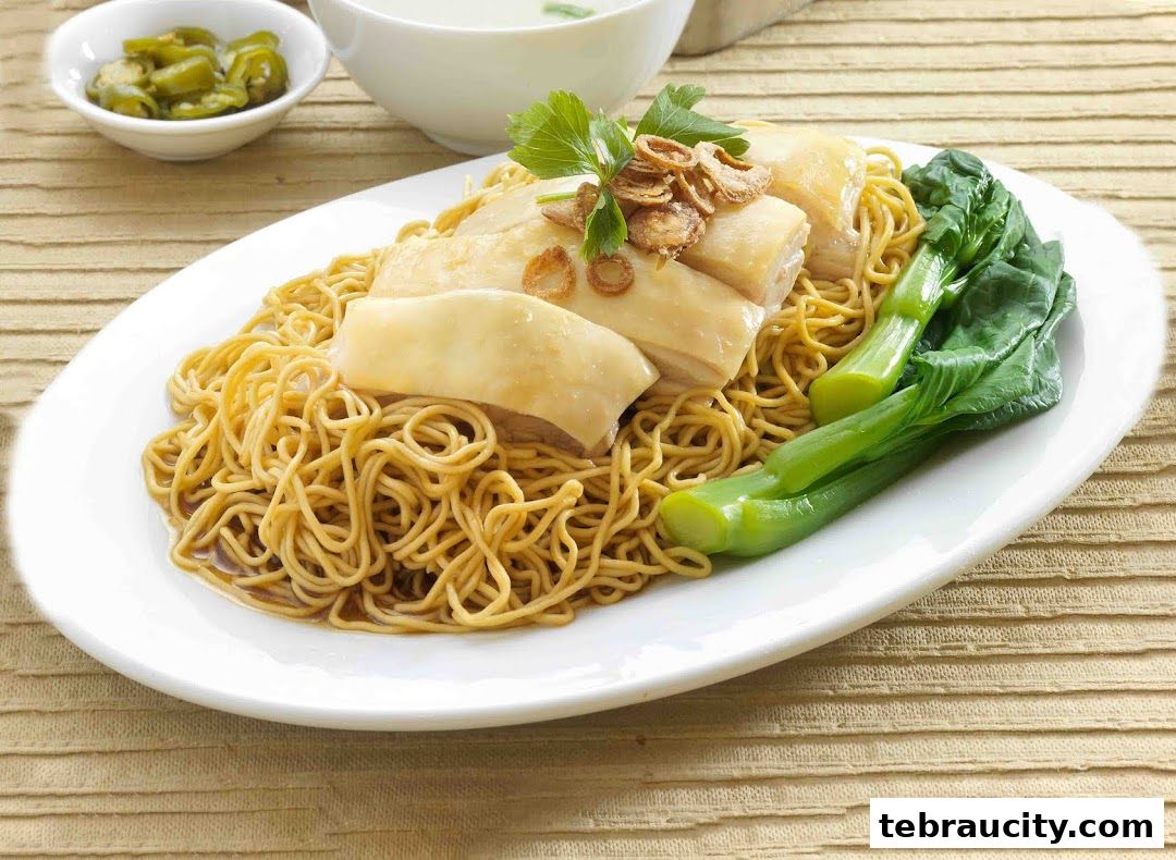 A plate of delicious chicken rice noodles with blanched greens and a side of chili.