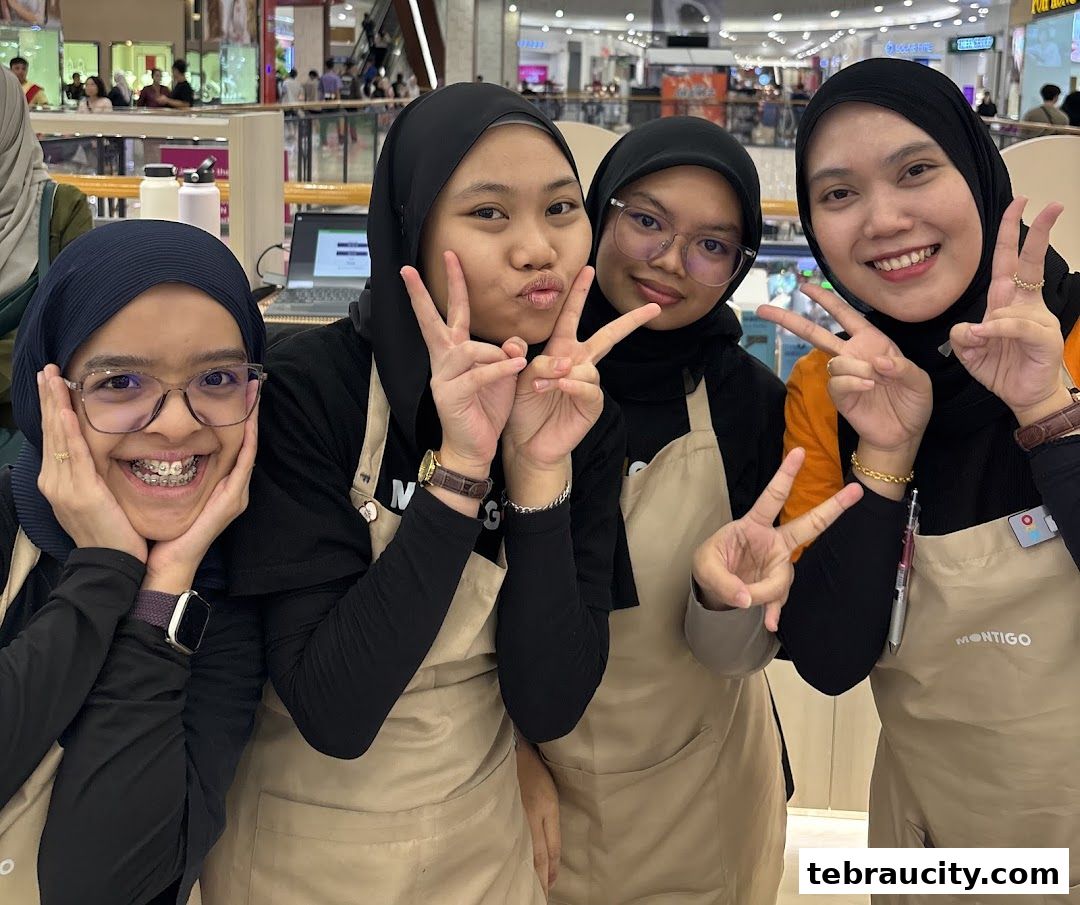 Four smiling young women wearing aprons and hijabs pose for a photo, making peace signs.