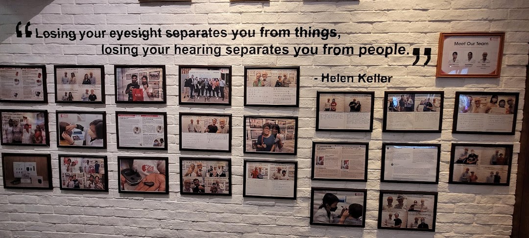 A white brick wall displays a Helen Keller quote about hearing, surrounded by framed photos of the team and customers.