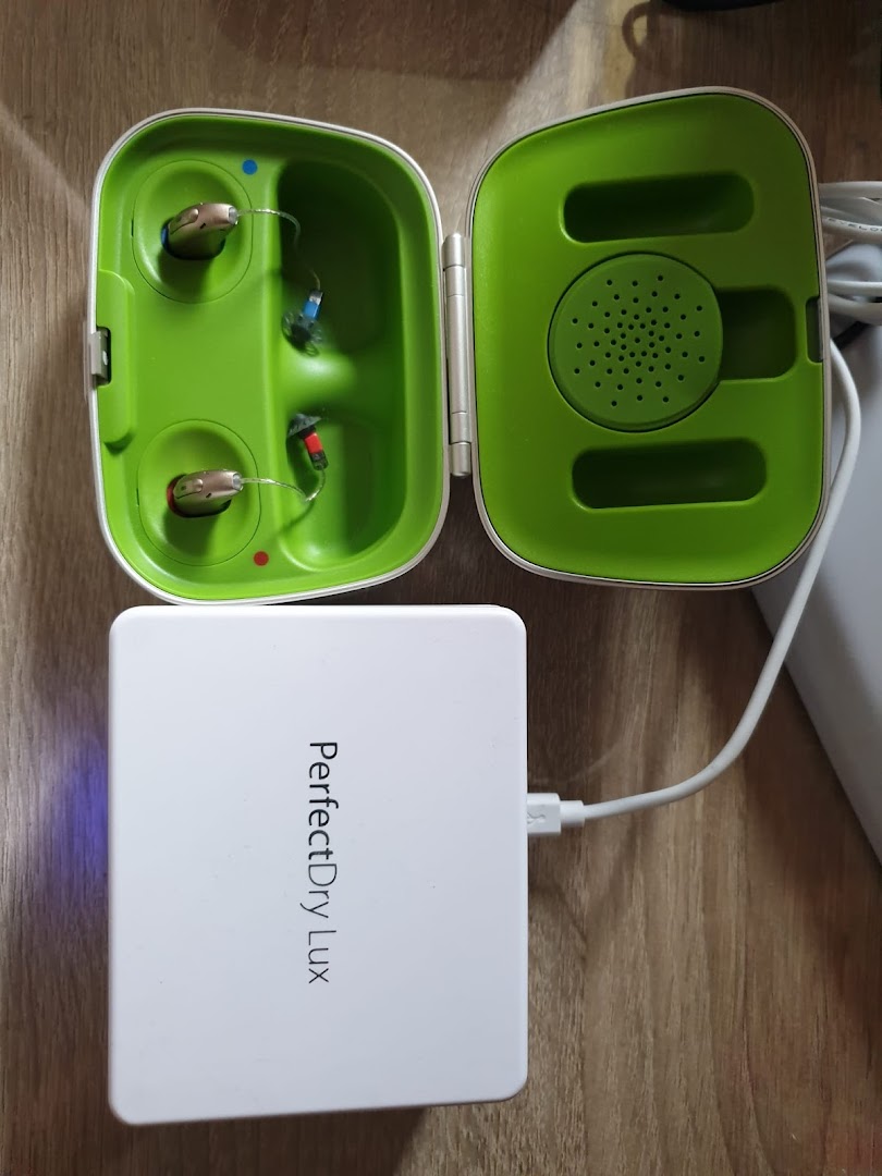 Two hearing aids in a green charging/drying case next to a white PerfectDry Lux drying unit.